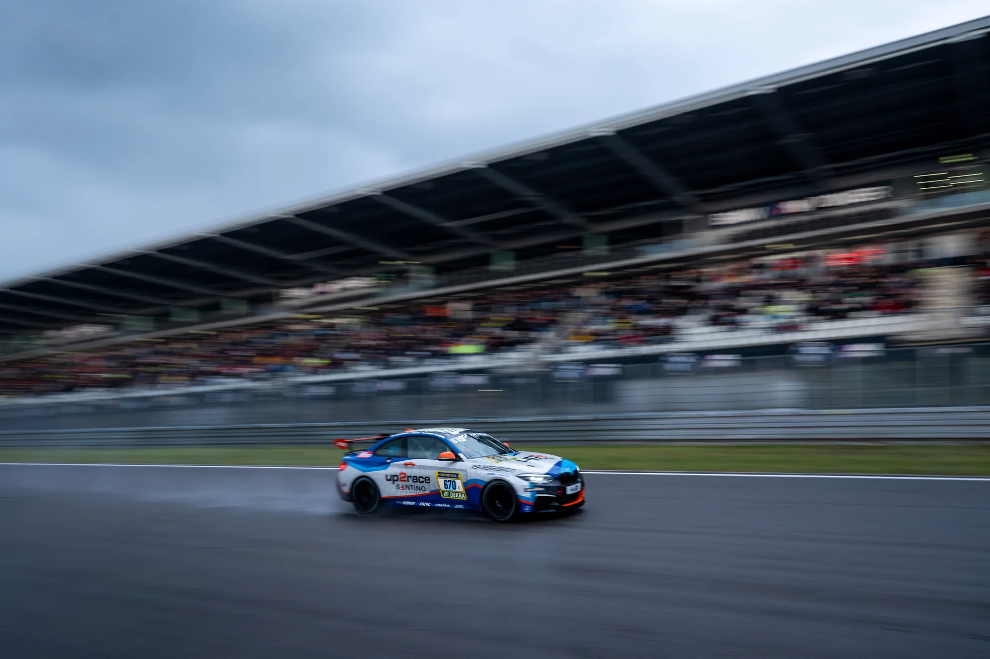 The BMW M240i Racing #670 on a wet track in front of the grandstand